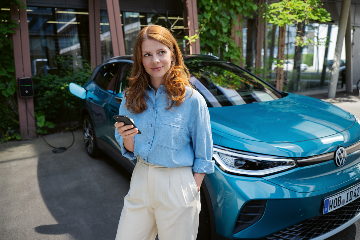 Frau mit Handy lehnt an einem blauen VW ID.4